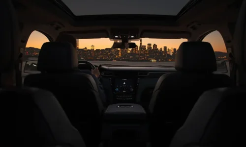 Rear passenger view inside a black luxury sedan approaching Manhattan at dusk with city skyline visible through the windshield